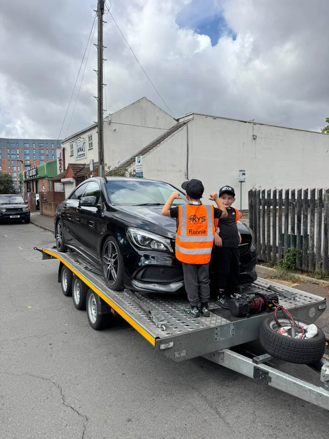 Two children wearing KYS Recovery clothing beside a recovered vehicle